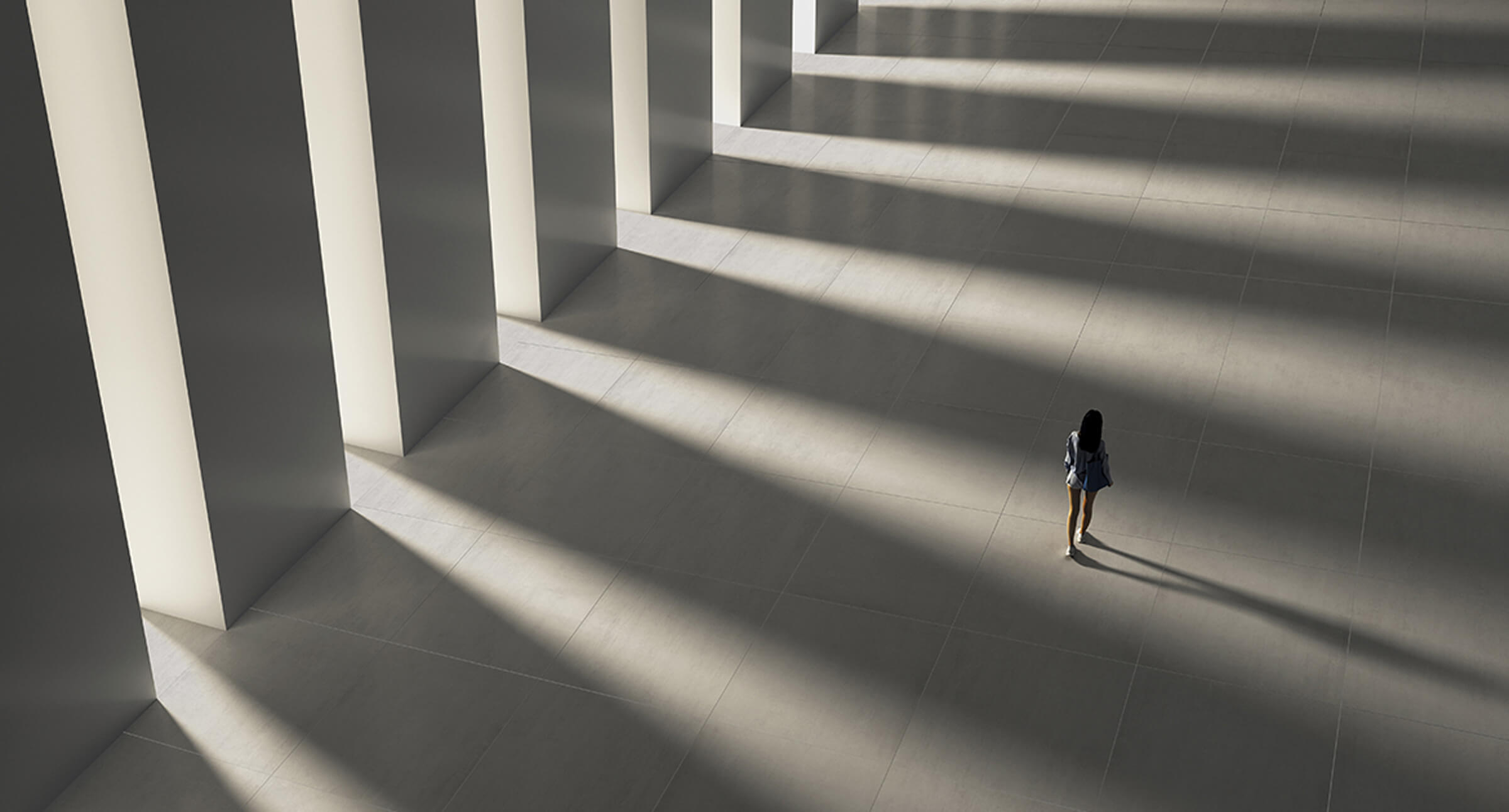 Woman walking through expansive hallway with large pillows and light flowing in.