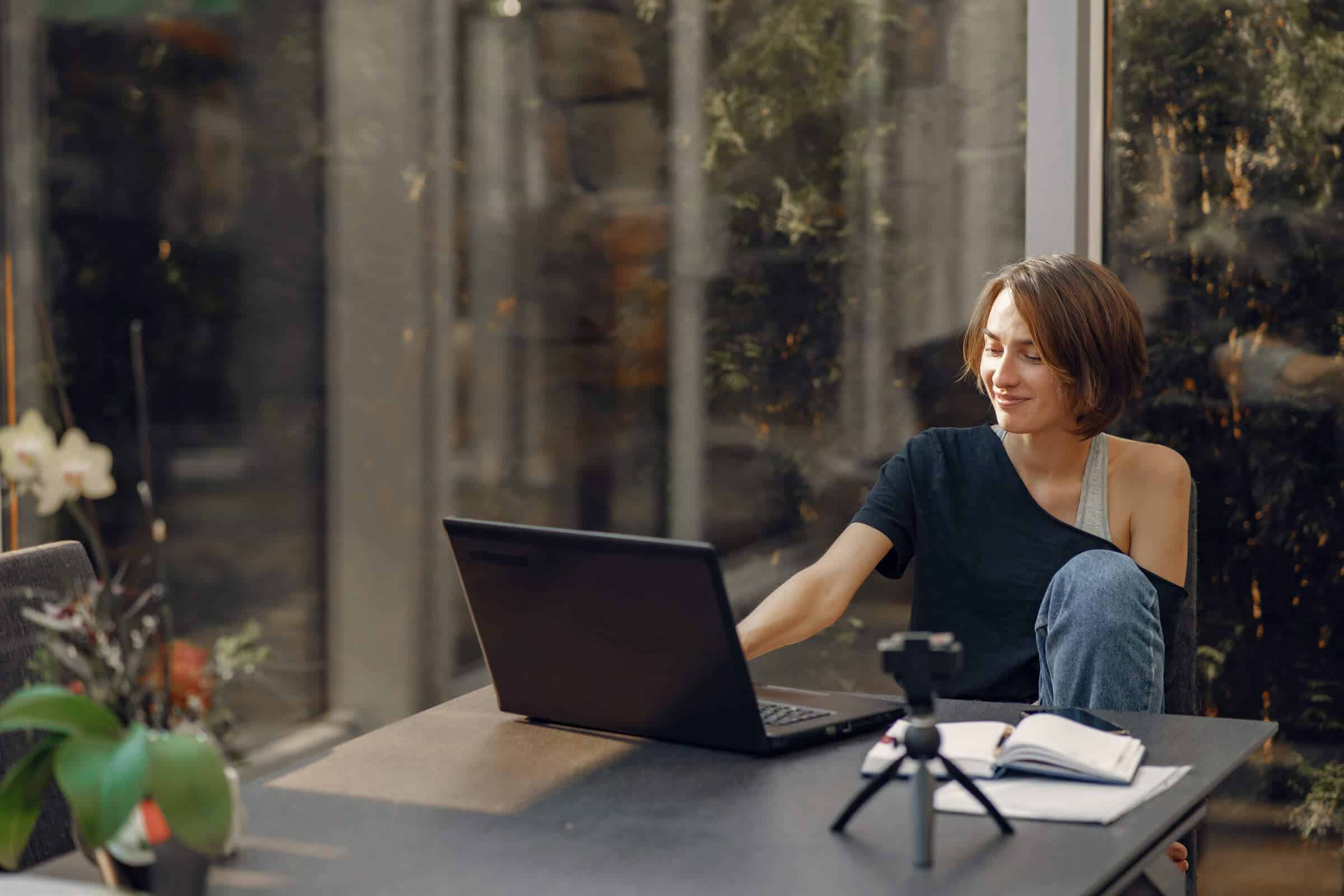 Individual working at desk with computer and tripod surrounded by large windows and plenty of nature.