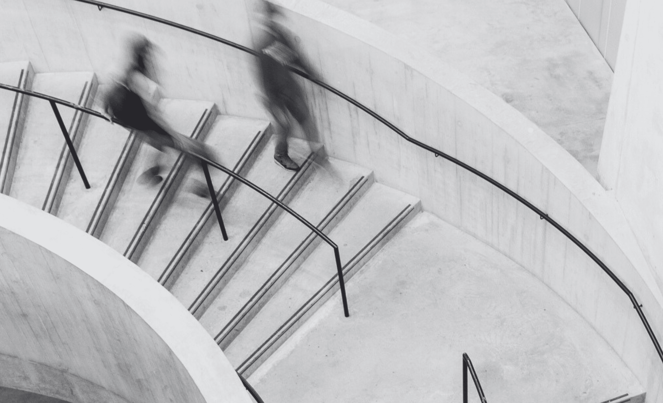 Black and white image of two people walking down spiral staircase in blurred motion.