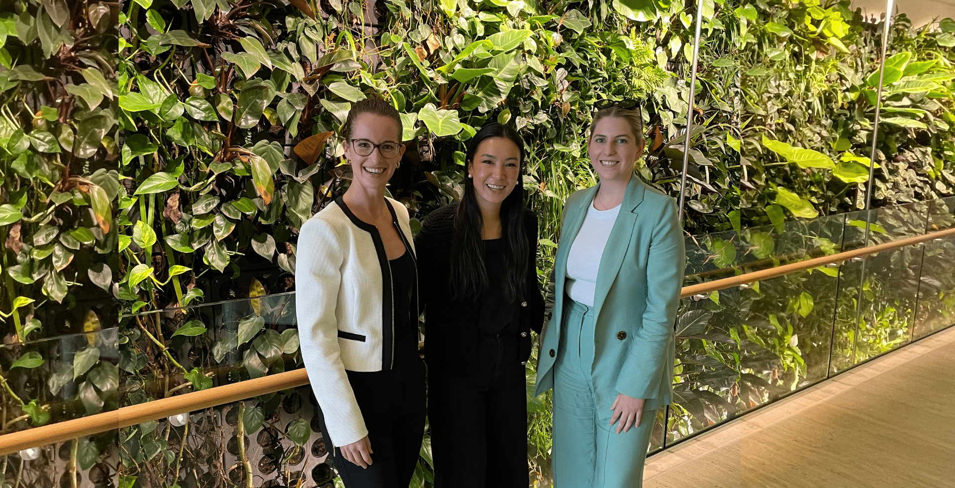 Spaceful team in work attire smiling in front of vertical wall.