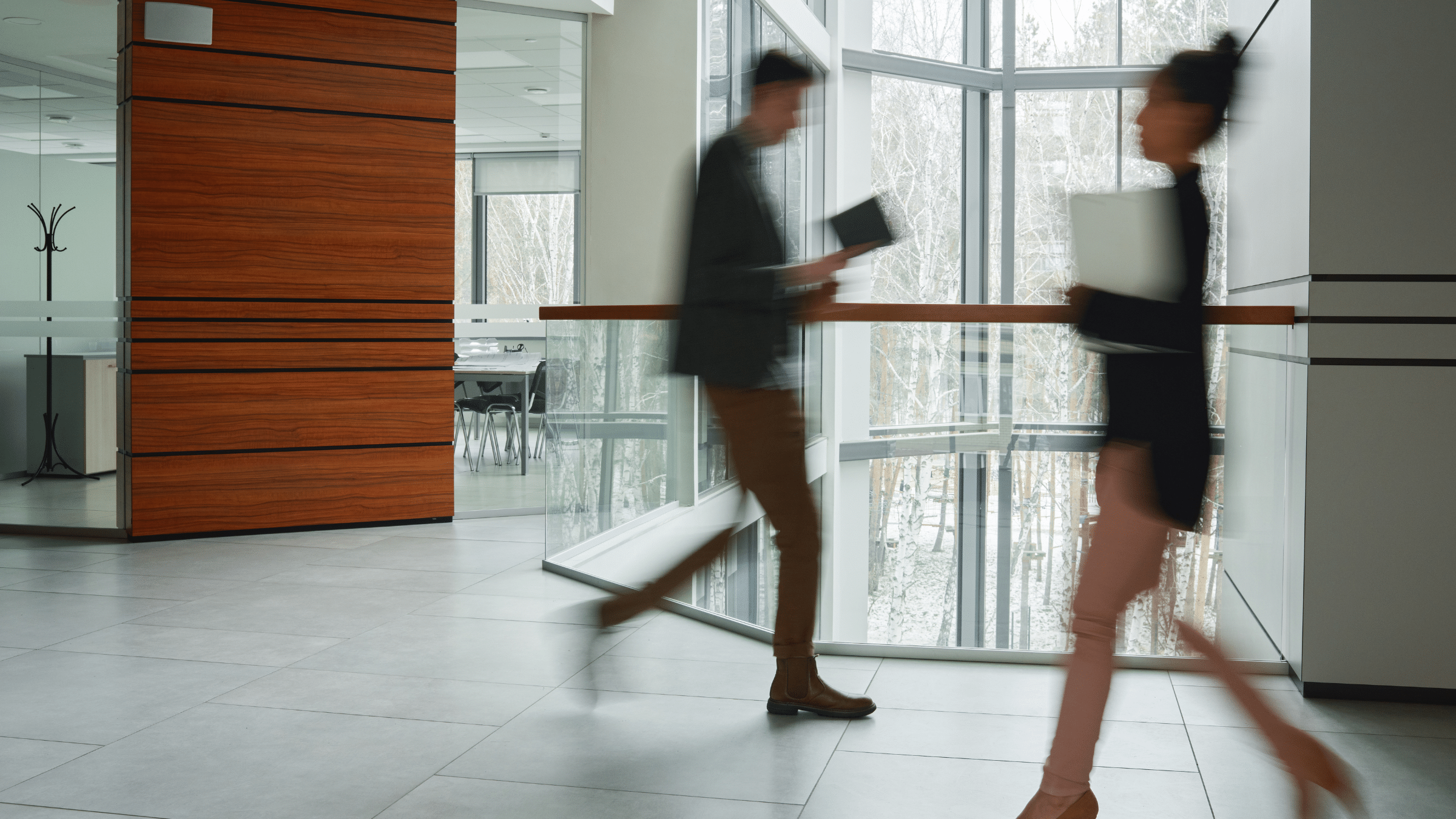 Two people walking in opposite directions through an office hallway.