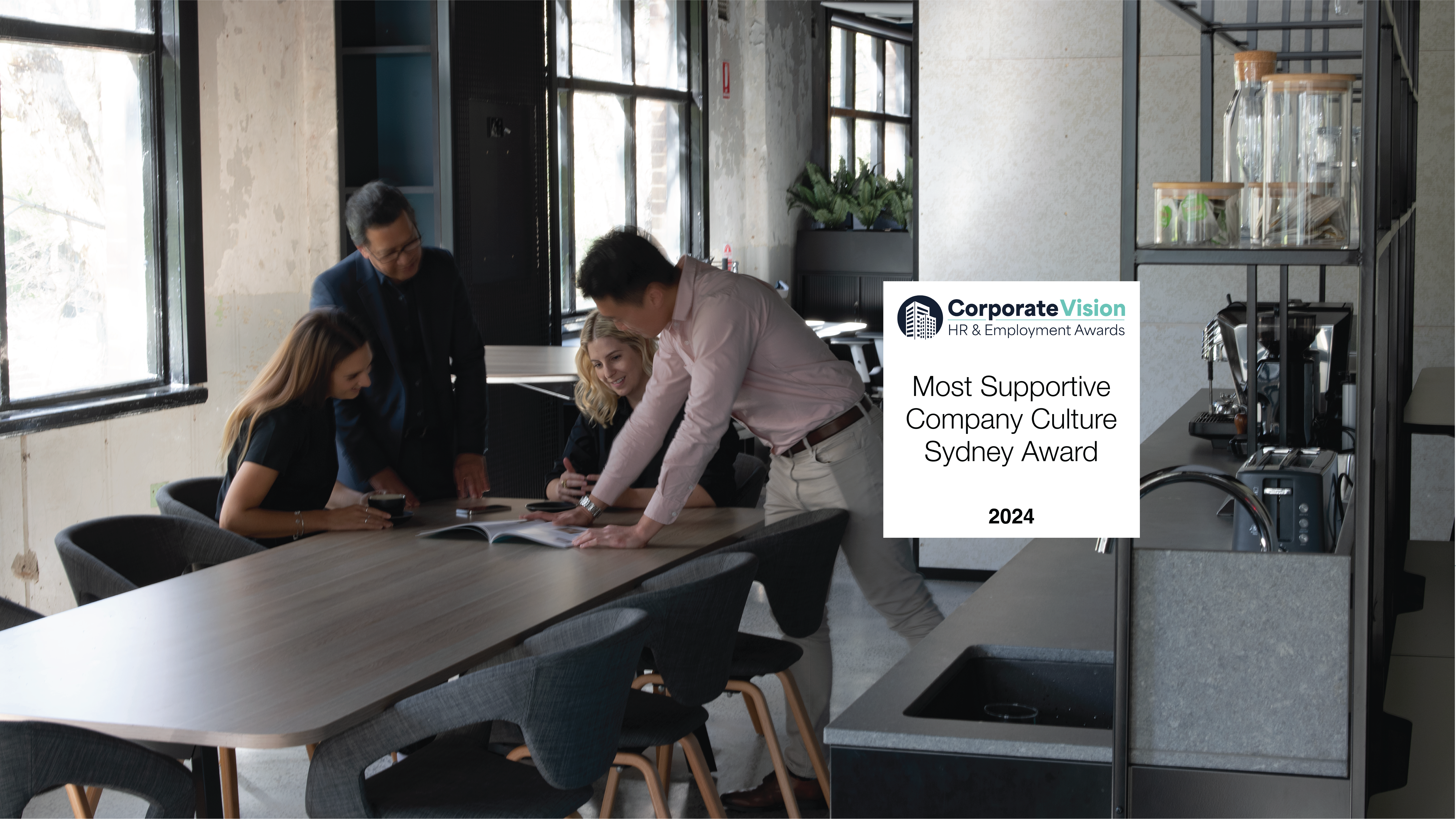 Four people working together, engaged in a collaborative discussion, with laptops and documents spread across the table.