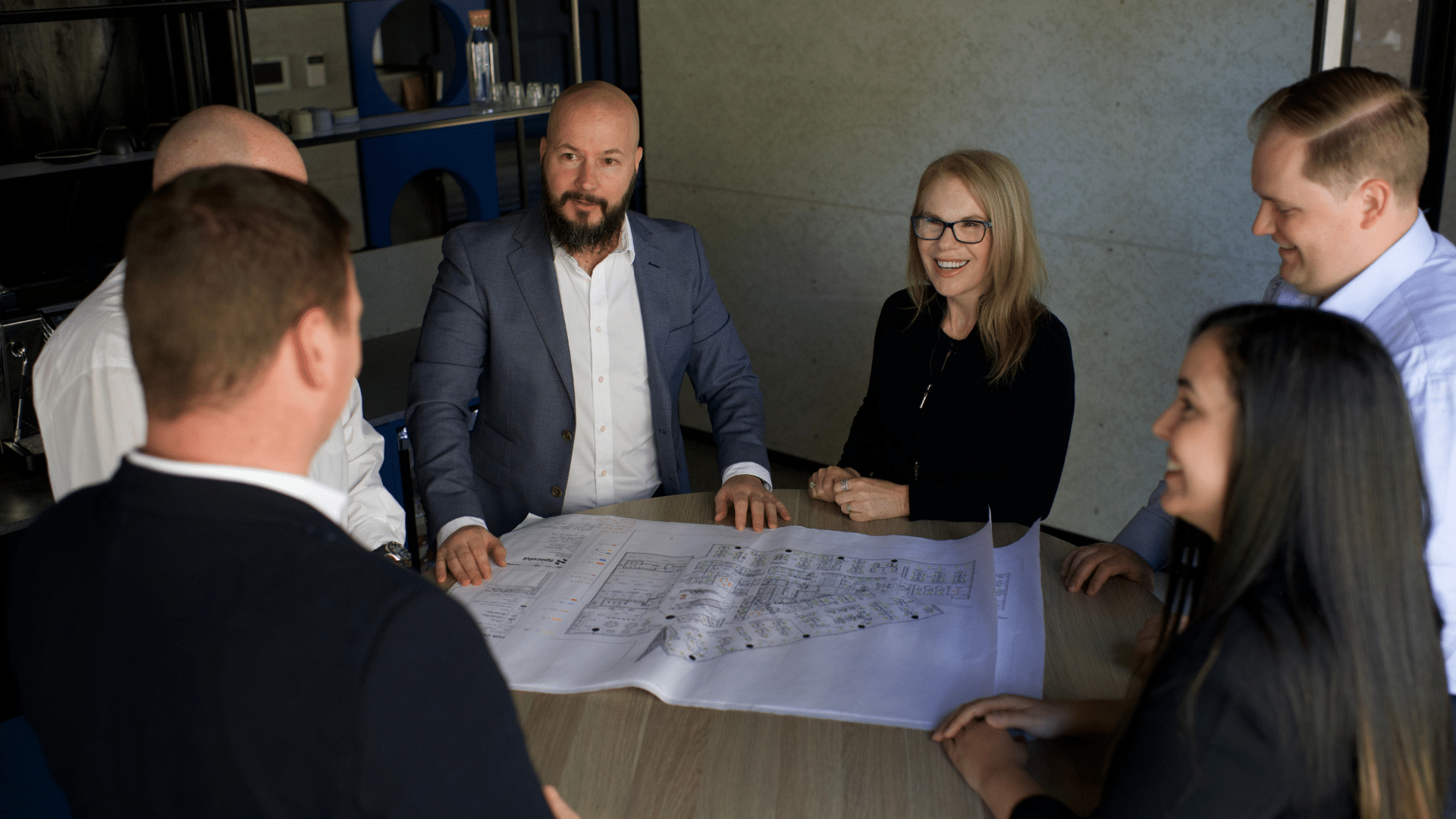 Six people working together, engaged in a collaborative discussion, with documents spread across the table.