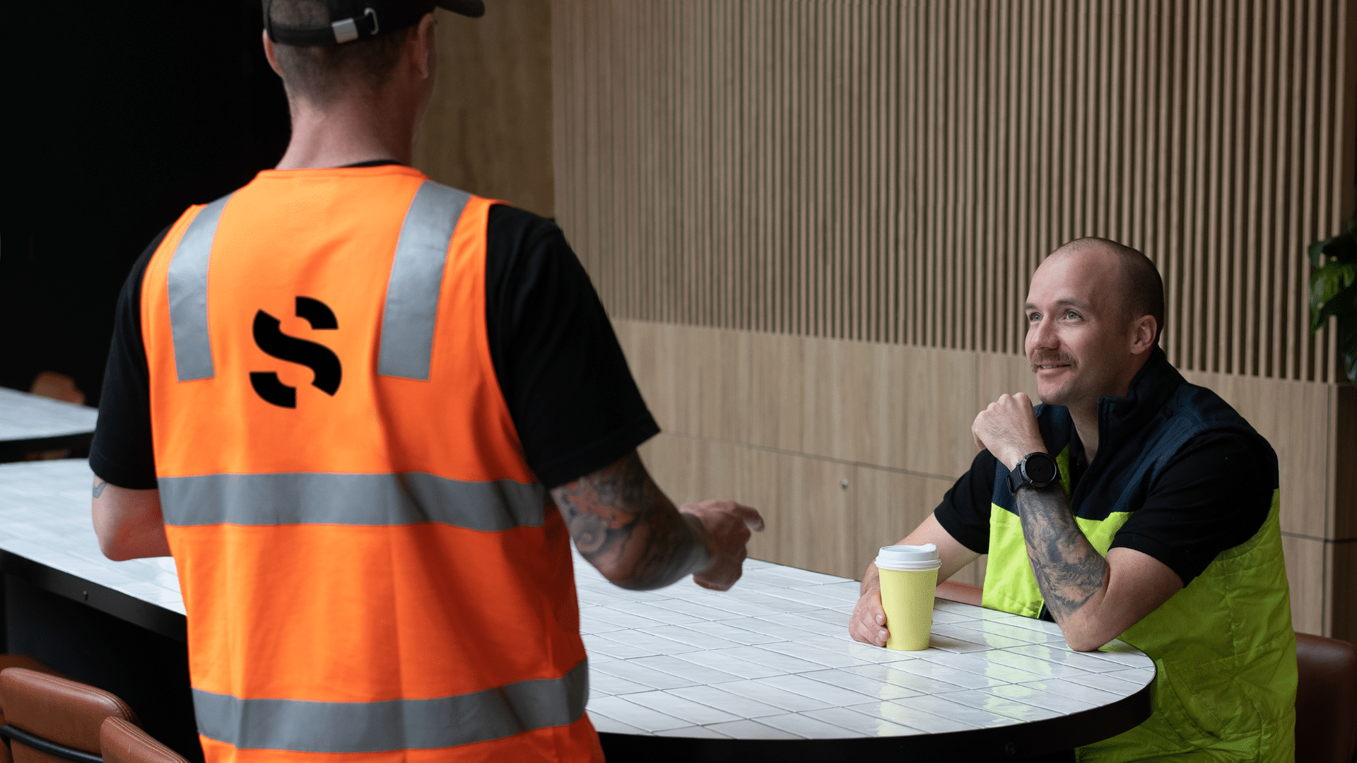 Construction workers wearing high vis vests having a discussion over a coffee.