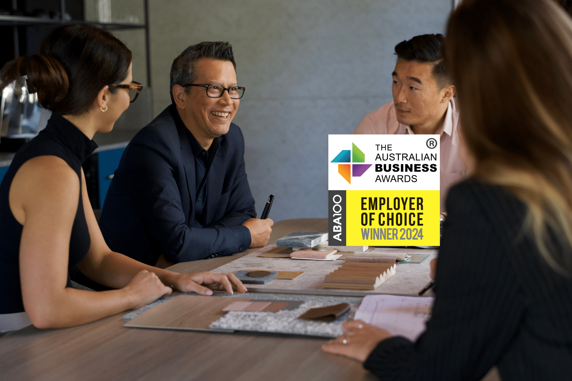Four people sitting around a table discussing samples and designs. Employer of Choice Winner of the Australian Business Awards in the foreground.