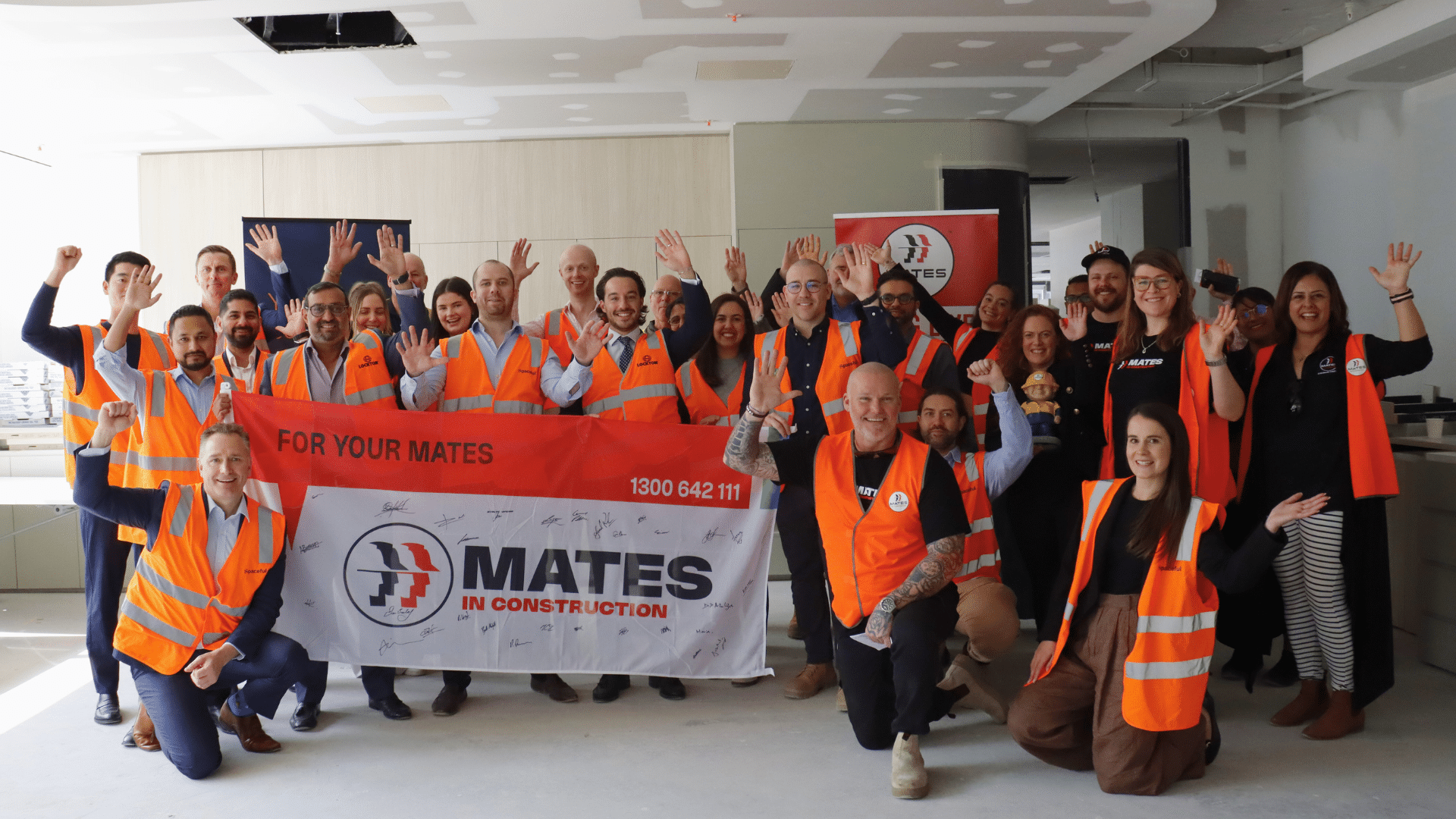 Team photo of the Spaceful onsite wearing safety gear and holding a Mates in Construction banner