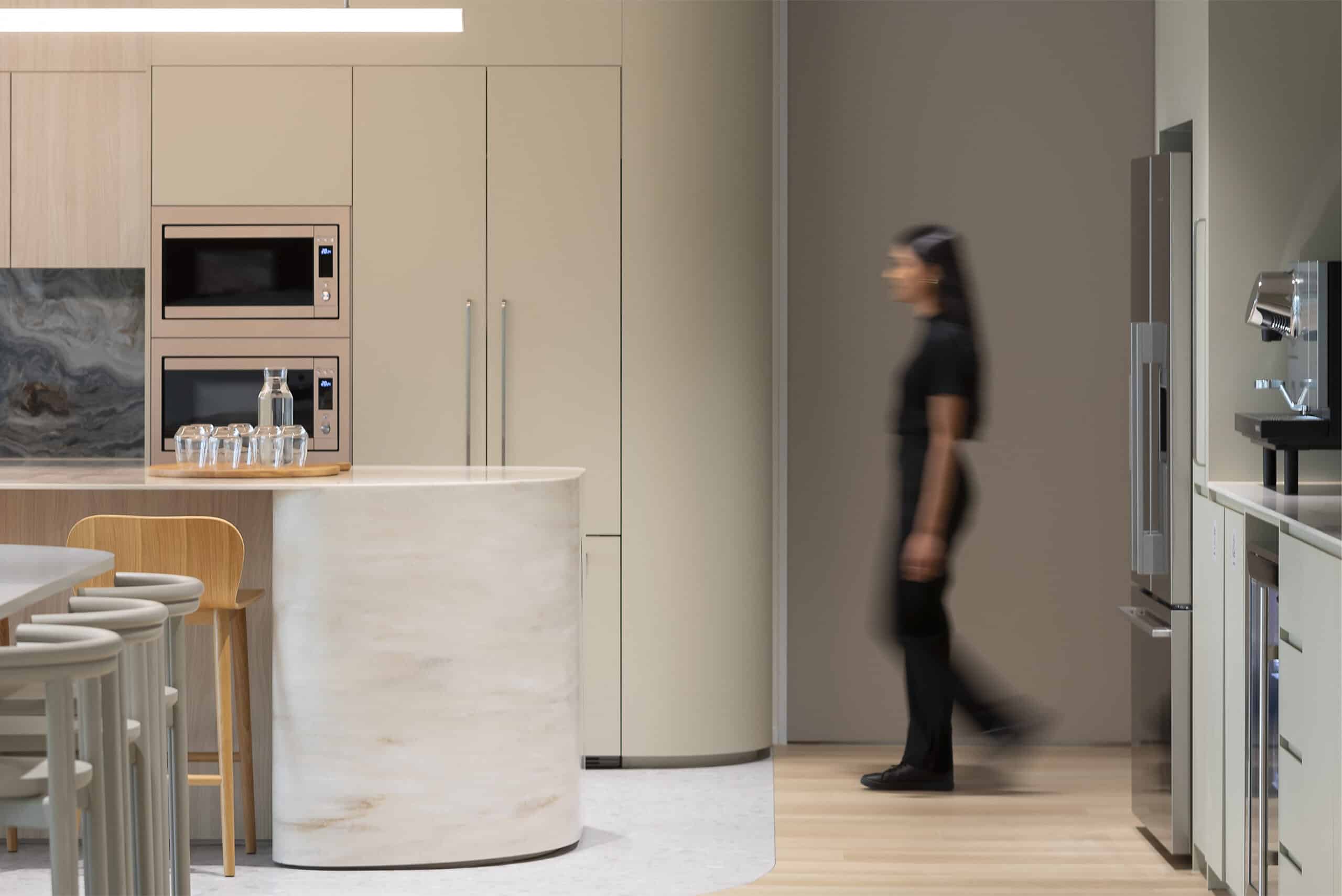 A contemporary kitchen space with high chairs lined along a sleek counter, large windows allowing ample natural light, and a stylish, open design for a welcoming atmosphere.