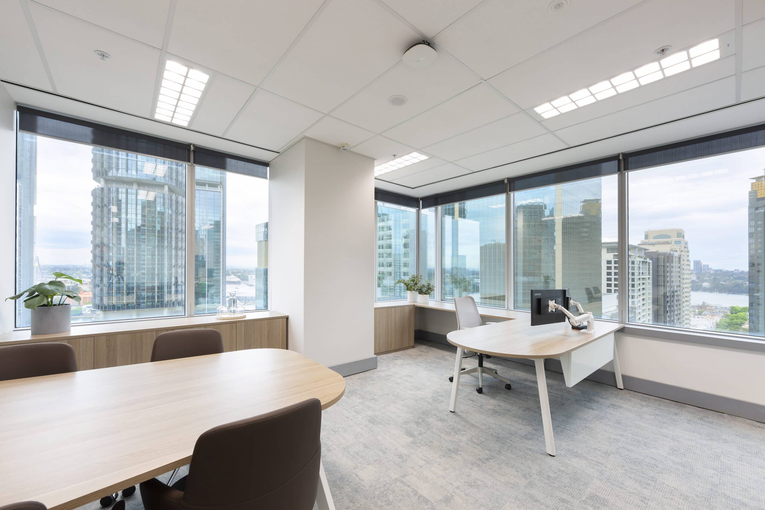 Modern office space with large windows providing ample natural light and desks with ergonomic chairs.